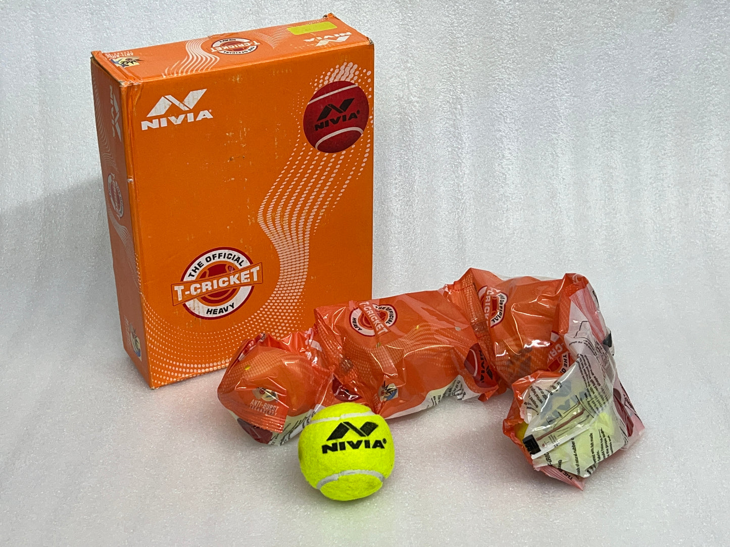 Pack of 12 Nivia Heavy Tennis Cricket Balls, in red or green, designed for cricket play with a hard tennis ball construction, made in India.